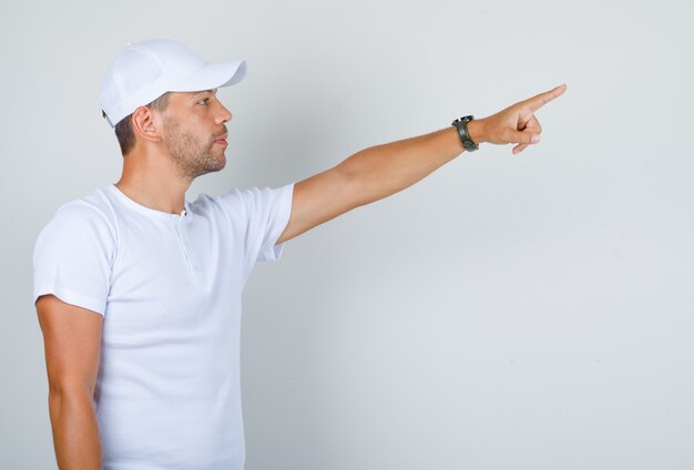 Młody człowiek wskazując palcem na coś w białej koszulce, czapce.