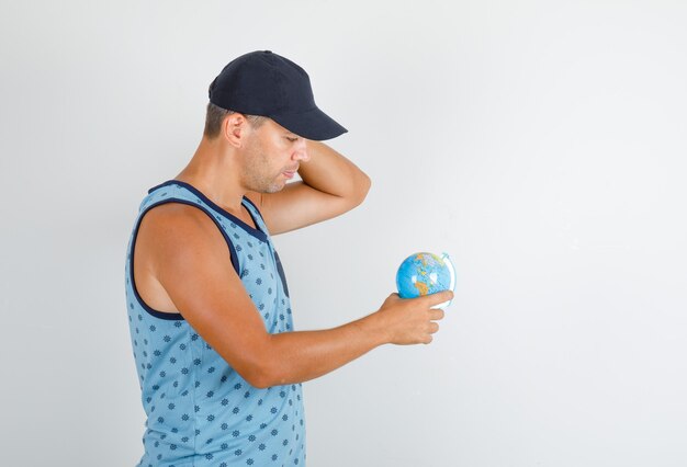 Młody człowiek wskazując palcem na świecie w niebieski podkoszulek z czapką i patrząc ostrożnie