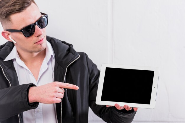 Młody człowiek wskazuje palec nad cyfrową stołową pozycją przeciw biel ścianie