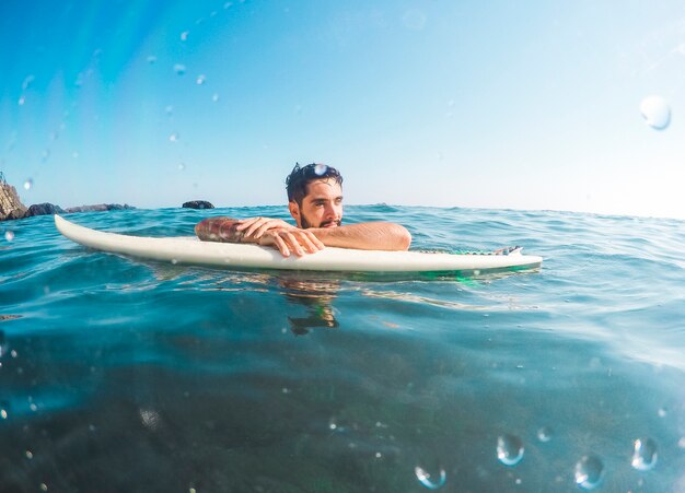 Młody człowiek z białym surfboard w błękitne wody