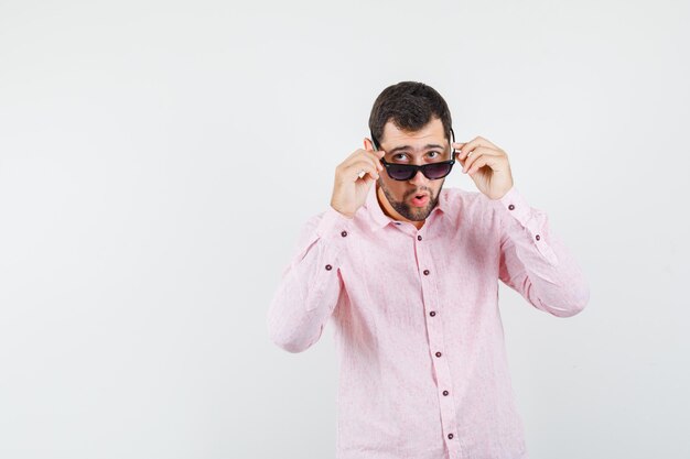 Młody człowiek zdejmując okulary w różowej koszuli i patrząc zaskoczony