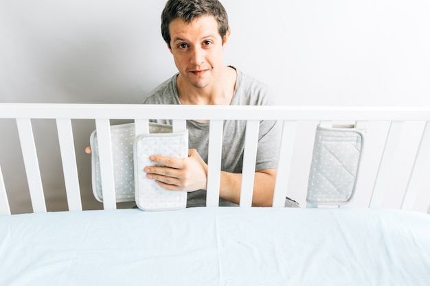 Młody dorosły mężczyzna instaluje błotniki w łóżeczku na przybycie dziecka. koncepcja spodziewa się nowego dziecka. rodzicielstwo i przygotowania