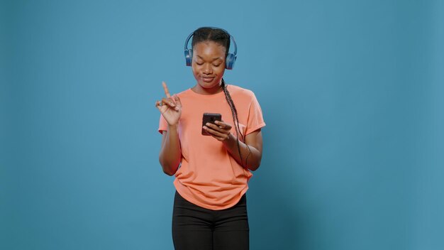 Młody dorosły ze słuchawkami wykonujący ruchy taneczne i zmieniający piosenkę za pomocą smartfona. Pozytywna osoba słuchająca muzyki na zestawie słuchawkowym i patrząca na ekran telefonu komórkowego, bawiąca się i tańcząca.