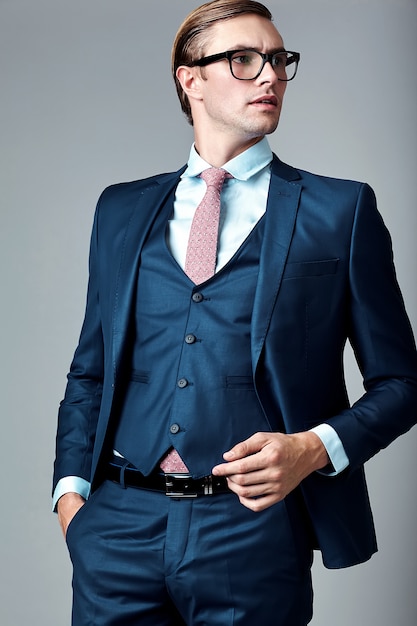 Młody elegancki przystojny biznesmen samiec model w błękitnym kostiumu i modnych szkłach pozuje w studiu