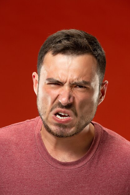 Młody emocjonalny gniewny mężczyzna krzyczy na czerwonej studio ścianie
