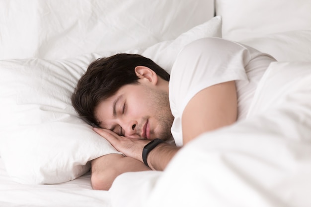 Młody facet śpi w łóżku na sobie smartwatch lub tracker snu