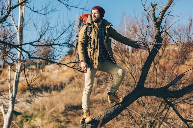 Młody hipster mężczyzna podróżujący z plecakiem w jesiennym lesie, ubrany w ciepłą kurtkę