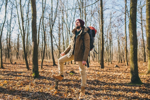 Młody hipster mężczyzna podróżujący z plecakiem w lesie jesienią na sobie ciepłą kurtkę i kapelusz, aktywny turysta, odkrywanie przyrody w zimnych porach roku