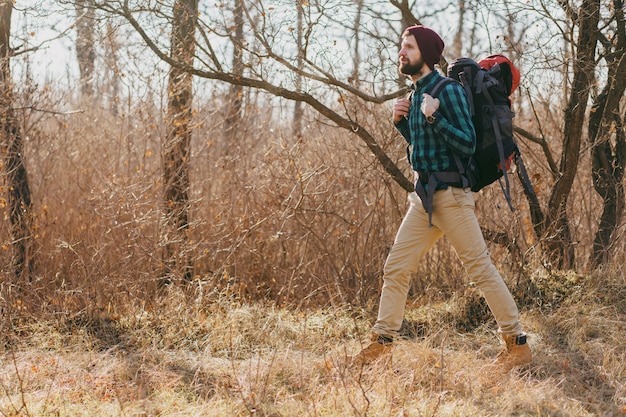 Młody hipster mężczyzna podróżujący z plecakiem w lesie jesienią na sobie koszulę w kratę i kapelusz, aktywny turysta spacerujący, odkrywanie przyrody w zimnych porach roku