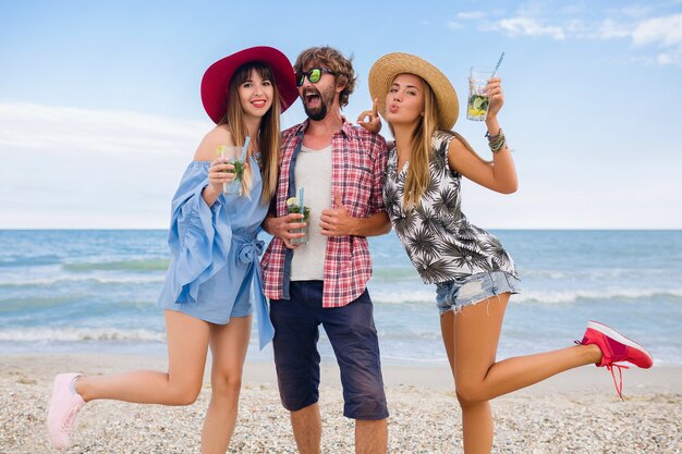 Młody hipster towarzystwo przyjaciół na wakacjach na plaży, pijąc koktajl mojito, szczęśliwy pozytywny, letni styl, uśmiechnięty szczęśliwy, dwie kobiety i mężczyzna bawią się razem, rozmawiają, flirt, romans, trzy