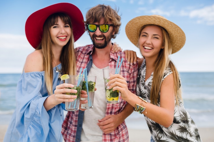 Bezpłatny plik Zdjęcie młody hipster towarzystwo przyjaciół na wakacjach na plaży, pijąc koktajl mojito, szczęśliwy pozytywny, letni styl, uśmiechnięty szczęśliwy, dwie kobiety i mężczyzna bawią się razem, rozmawiają, flirt, romans, trzy
