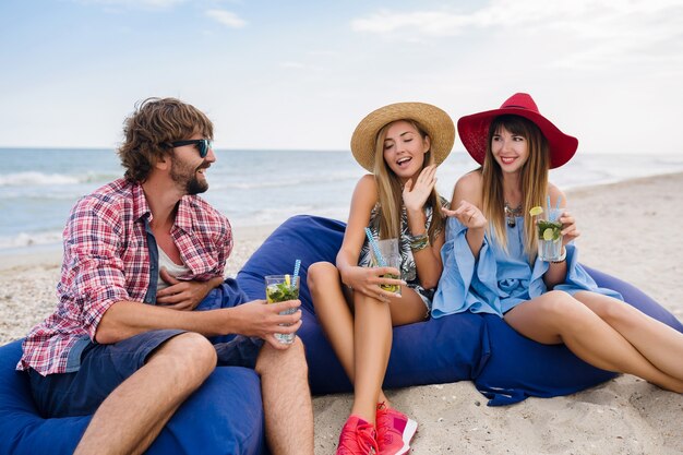 Młody hipster towarzystwo przyjaciół na wakacjach w kawiarni na plaży, pijąc koktajl mojito, szczęśliwy pozytywny, letni styl, uśmiechnięty szczęśliwy, dwie kobiety i mężczyzna bawią się razem, rozmawiają, flirt, romans, trzy