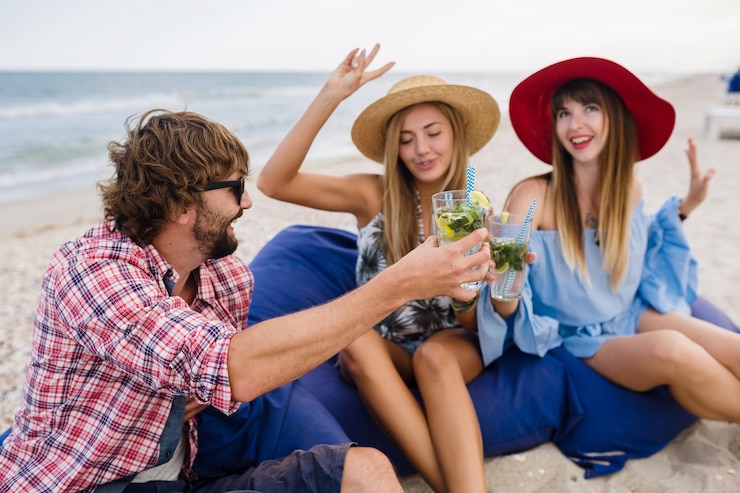 Bezpłatny plik Zdjęcie młody hipster towarzystwo przyjaciół na wakacjach w kawiarni na plaży, pijąc koktajl mojito, szczęśliwy pozytywny, letni styl, uśmiechnięty szczęśliwy, dwie kobiety i mężczyzna bawią się razem, rozmawiają, flirt, romans, trzy