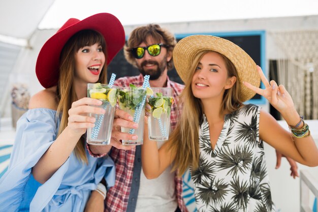 Młody hipster towarzystwo przyjaciół na wakacjach w letniej kawiarni, picie koktajli mojito, szczęśliwy pozytywny styl, uśmiechnięty szczęśliwy, dwie kobiety i mężczyzna bawią się razem, rozmawiają, flirt, romans, trzy