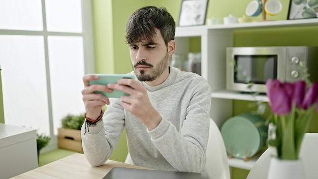 Bezpłatne zdjęcie młody hiszpański mężczyzna grający w gry wideo za pomocą smartfona w jadalni