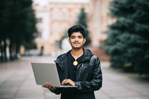 Młody indyjski mężczyzna stać plenerowy z laptopem z przodu