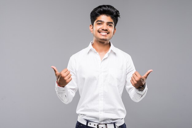 Młody indyjski mężczyzna stoi nad odosobnioną szarości ścianą zatwierdza robić pozytywnemu gestowi z ręką, aprobatami uśmiechniętymi i szczęśliwymi dla sukcesu