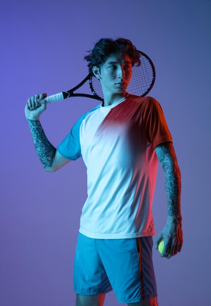 Młody kaukaski mężczyzna grający w tenisa na fioletowym tle studio w neonowej akcji i koncepcji ruchu
