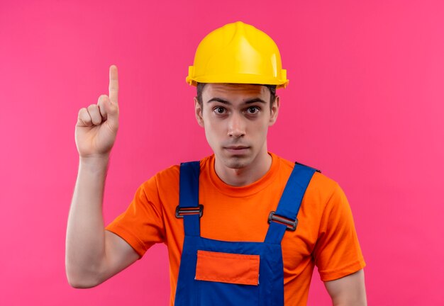 Młody konstruktor mężczyzna ubrany w mundur konstrukcyjny i kask ochronny wskazuje kciuk w górę