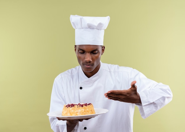 Młody Kucharz Afro-amerykański W Mundurze Szefa Kuchni Trzyma Ciasto Na Talerzu I Wskazuje Ręką Na Białym Tle Na Zielonym Tle Z Miejsca Na Kopię