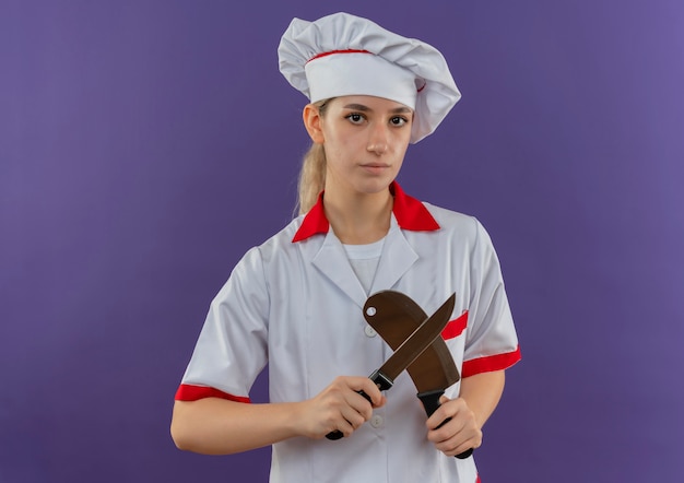 Młody ładny kucharz w mundurze szefa kuchni trzymając nóż i tasak patrząc