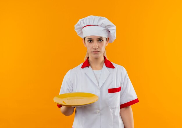 Młody ładny kucharz w mundurze szefa kuchni trzymając pusty talerz patrząc