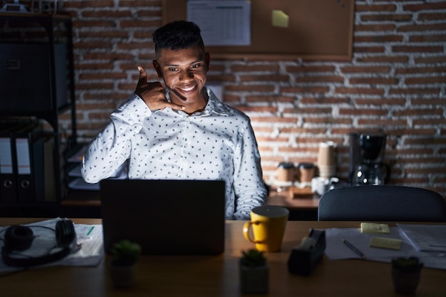 Młody latynos pracujący w biurze w nocy uśmiecha się, wykonując gest telefoniczny ręką i palcami, jak rozmawiając przez telefon, komunikując koncepcje