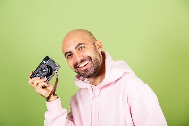Młody łysy mężczyzna kaukaski w różową bluzę z kapturem na białym tle, pozytywne hipster trzymać aparat