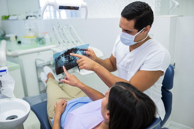 Młody męski dentysta egzamininuje promieniowanie rentgenowskie z żeńskim pacjentem