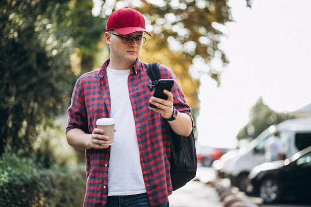 Młody męski uczeń pije kawę używać telefon w parku