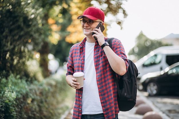 Młody męski uczeń pije kawę używać telefon w parku