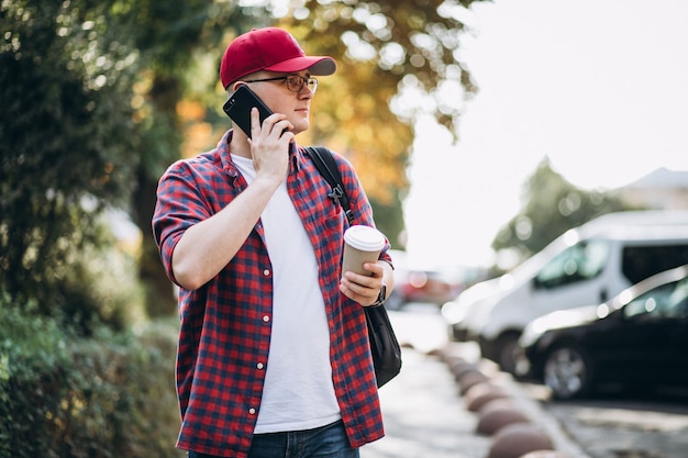 Bezpłatne zdjęcie młody męski uczeń pije kawę używać telefon w parku