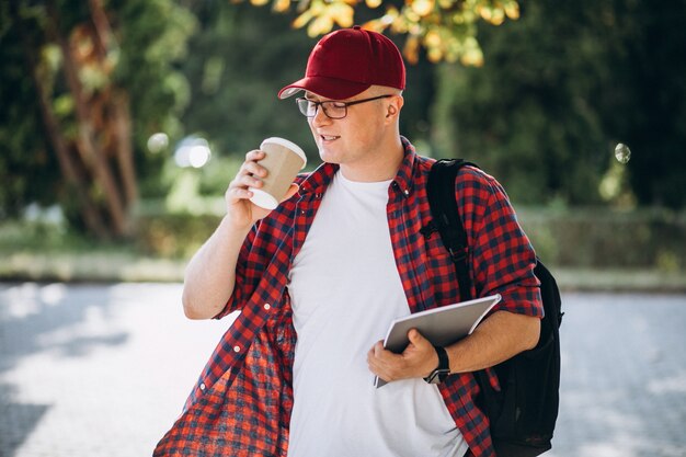 Młody męski uczeń pije kawę z laptopem w parku