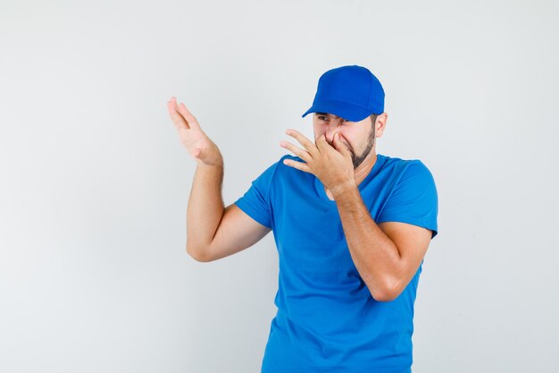 Młody mężczyzna czuje nieprzyjemny zapach w niebieskiej koszulce i czapce i wygląda na zniesmaczonego