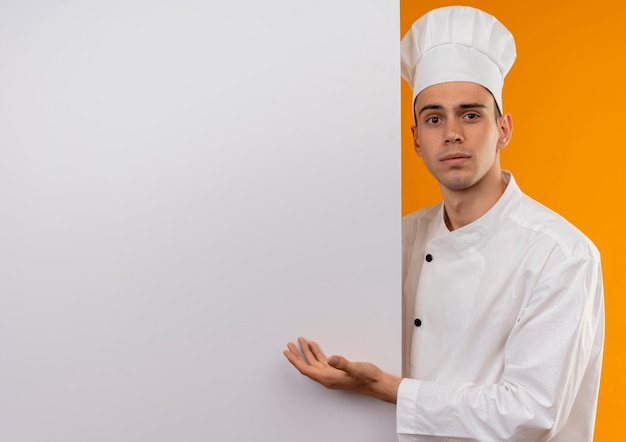 młody mężczyzna fajny ubrany w mundur szefa kuchni wskazuje ręką na białej ścianie na izolowanej żółtej ścianie z miejsca na kopię