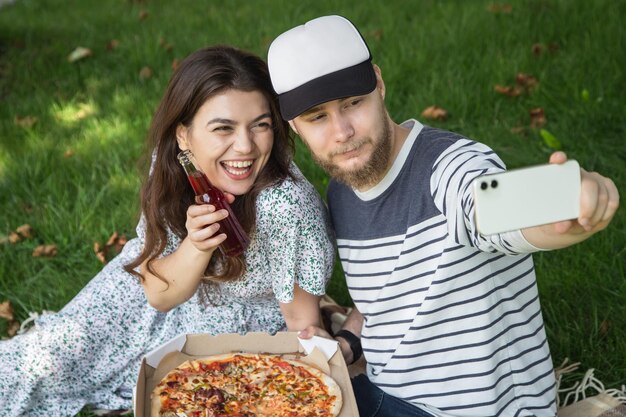 Młody mężczyzna i kobieta robią sobie selfie z pizzą na pikniku