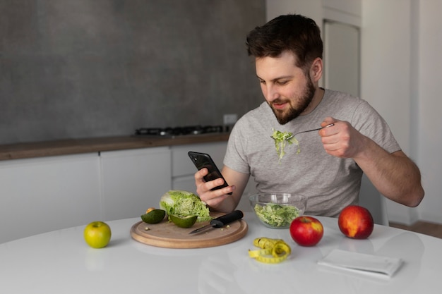 Bezpłatne zdjęcie młody mężczyzna je i sprawdza swój smartfon