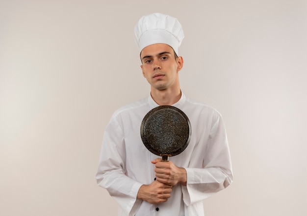 młody mężczyzna kucharz ubrany w mundur szefa kuchni trzymając patelnię na pojedyncze białe ściany z miejsca na kopię