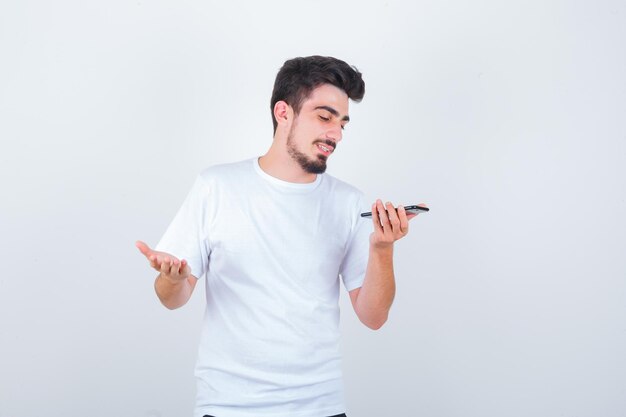 Młody mężczyzna nagrywający wiadomość głosową na telefonie komórkowym w koszulce i wyglądający wesoło