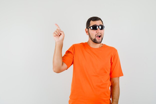 Młody mężczyzna palcem wskazującym w pomarańczowy t-shirt widok z przodu.