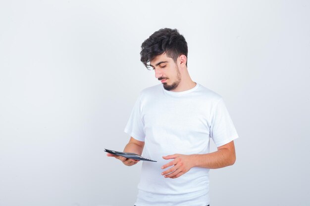 Młody mężczyzna patrzący na portfel w białej koszulce i patrzący zamyślony