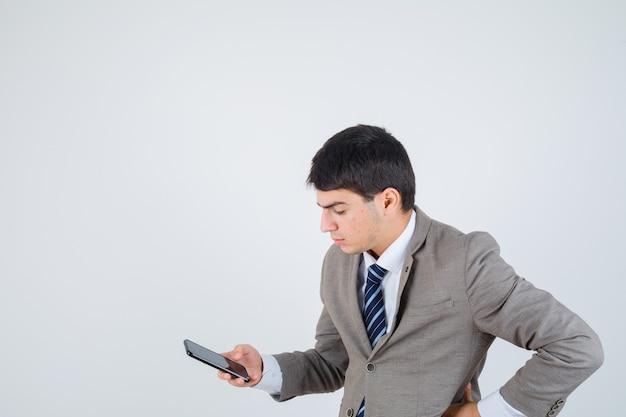 Młody mężczyzna patrzący na telefon, trzymający rękę na biodrze w formalnym garniturze