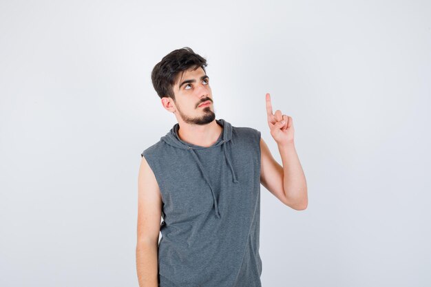 Młody mężczyzna podnoszący palec wskazujący w geście eureka w szarej koszulce i patrzący poważnie