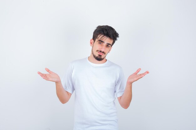 Młody mężczyzna pokazujący bezradny gest w białej koszulce i wyglądający na zdezorientowanego
