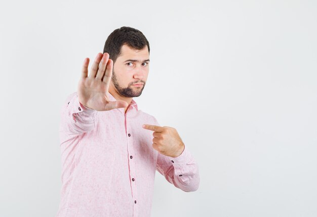 Młody mężczyzna pokazujący gest odmowy, wskazujący na siebie w różowej koszuli i wyglądający poważnie