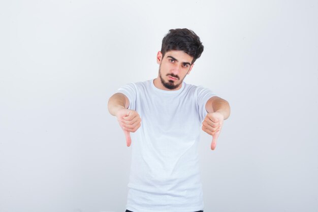 Młody mężczyzna pokazujący podwójne kciuki w dół w białej koszulce i wyglądający pewnie