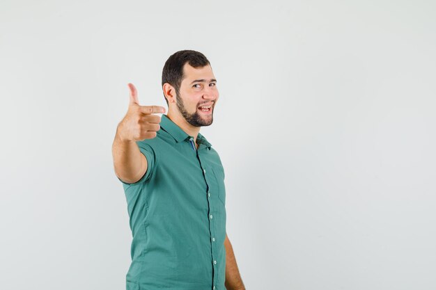 Młody mężczyzna pokazuje kciuk w zielonej koszuli i wygląda na zadowolony. przedni widok.