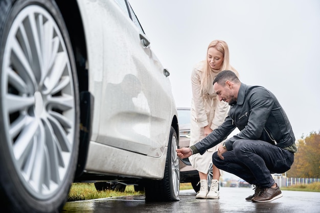 Bezpłatne zdjęcie młody mężczyzna pomaga uroczej kobiecie naprawić koło samochodu