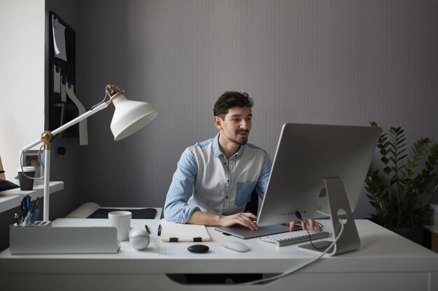 Młody mężczyzna projektant za pomocą tabletu graficznego podczas pracy z com