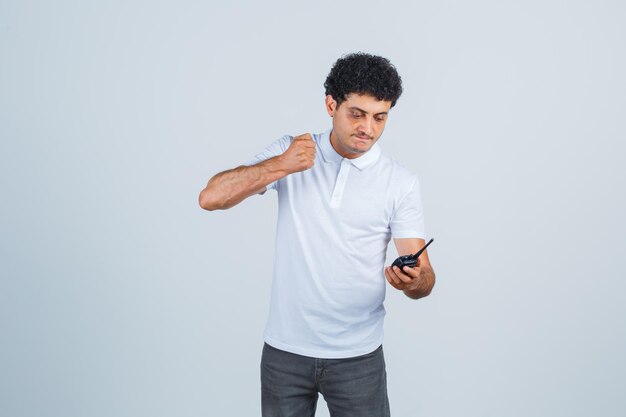 Młody mężczyzna przygotowuje się do uderzenia na telefon walkie talkie w białej koszulce, spodniach i wygląda na zirytowaną, widok z przodu.